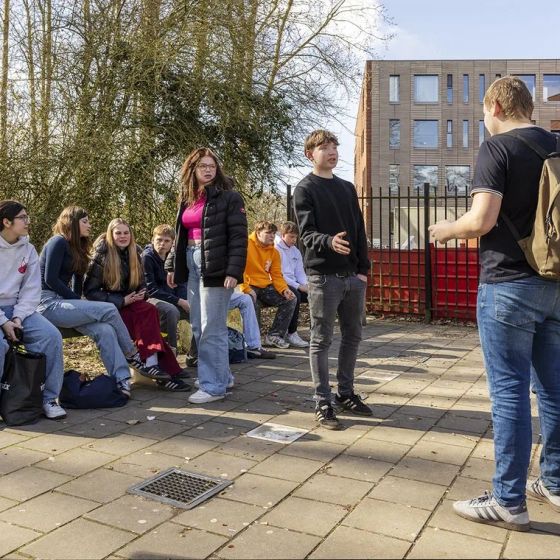 Studenten zitten en staan buiten bij een schoolgebouw terwijl een medestudent het woord voert