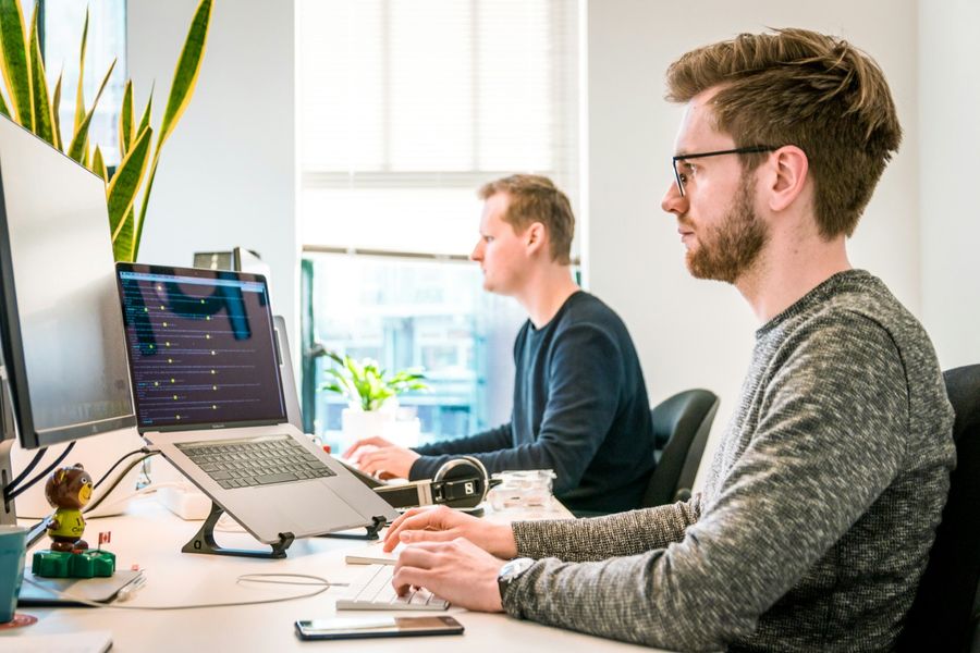 Twee developers aan het werk achter hun schermen, met code op een laptop