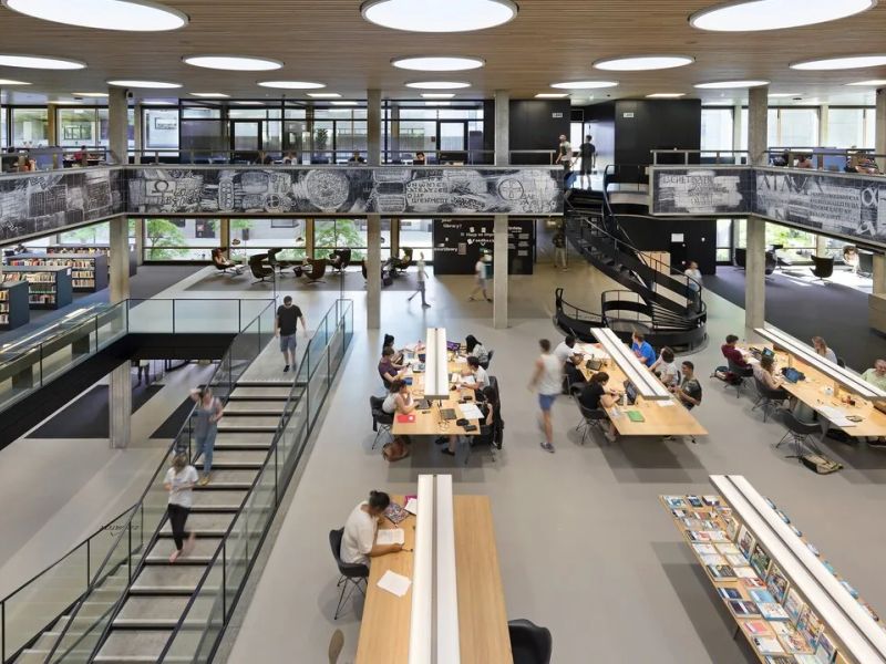 Students studying at long desks in a double-height university library