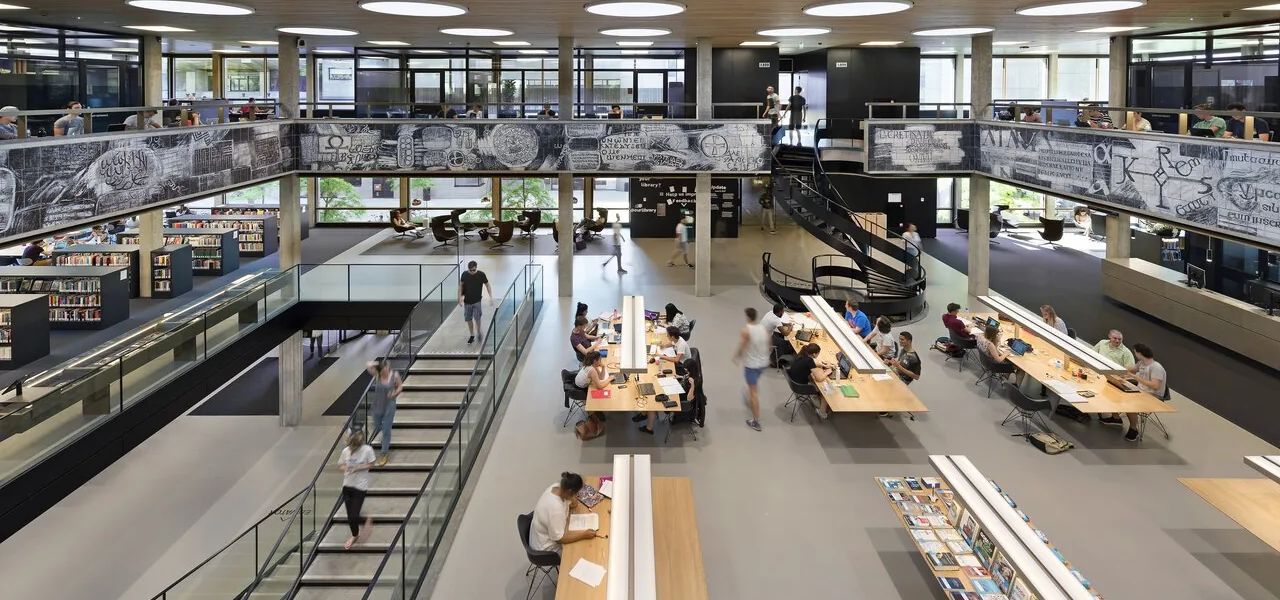 Students studying at long desks in a double-height university library