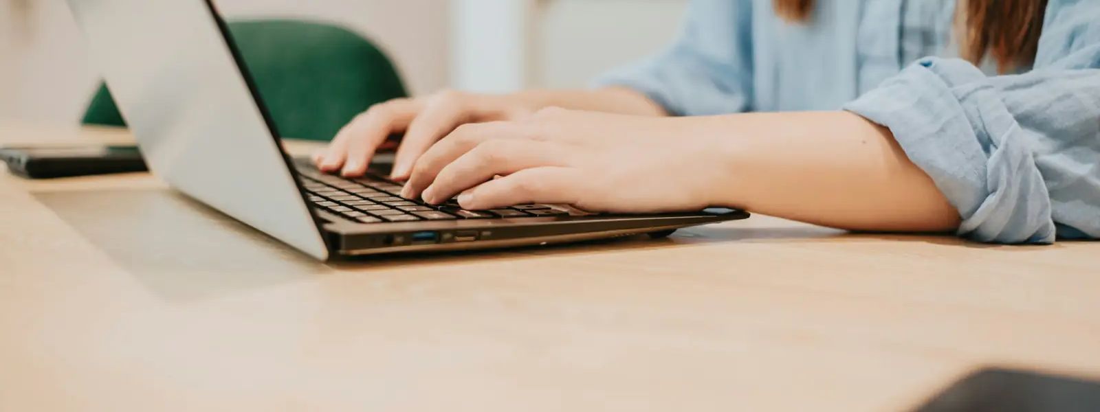 Close-up of hands typing on a laptop at a wooden table