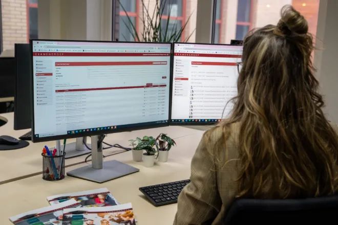 An Examengroep employee working with the exam platform open on two monitors