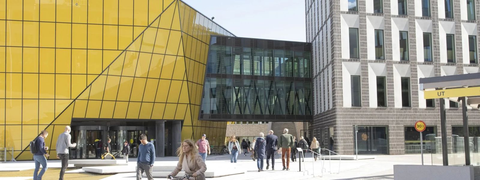 People walking and cycling past the yellow glass facade of the Linnaeus University building