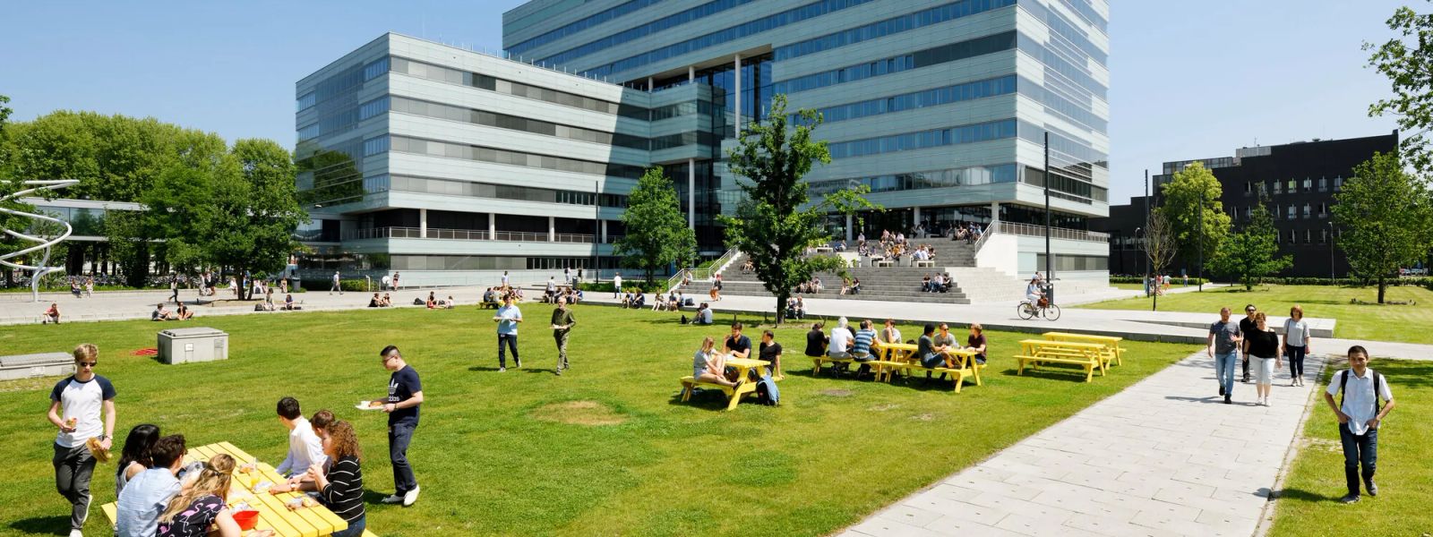 Students at yellow picnic tables on the lawn in front of a TU Eindhoven campus building