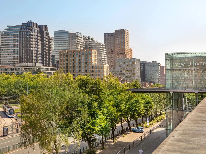 The glass facade of the Vrije Universiteit Amsterdam with the Zuidas skyline behind it
