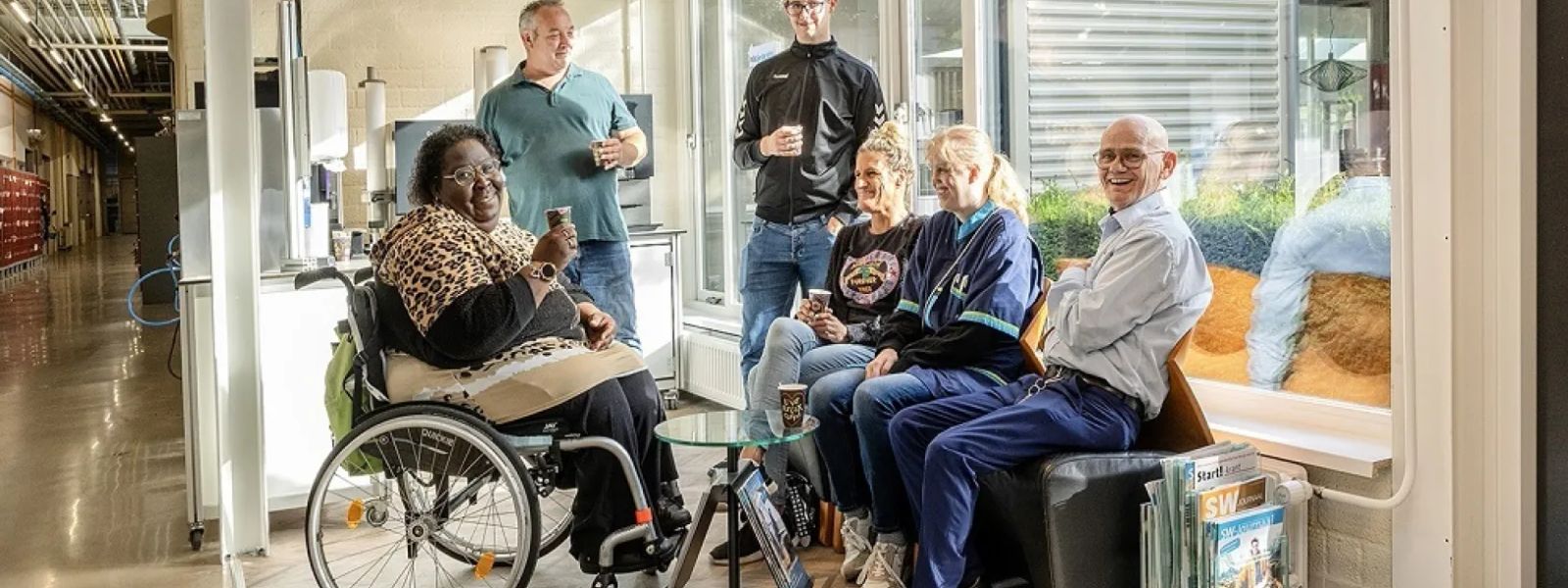 Colleagues taking a coffee break together in a WSD workplace, one of them using a wheelchair